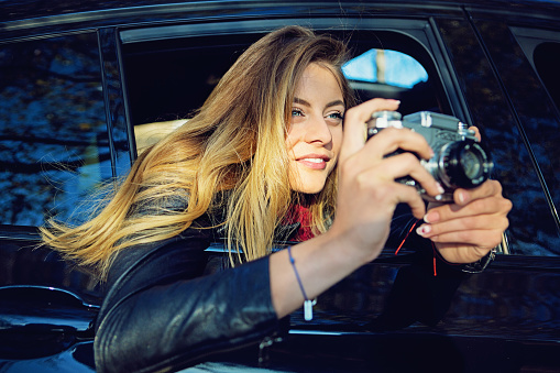 Beautiful girl is taking pictures with an old camera from the car