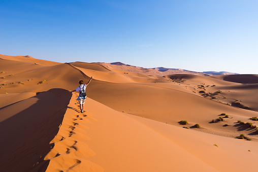 Man in short pants, walking, following the footprints on sand in Wahabi desert in Oman. In background is sand and sky.