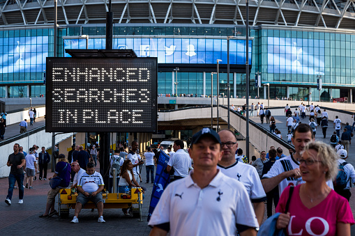 London, UK - September 14, 2016: supporters of Tottenham Hotspur FC wait on Wembley Way, outside Wembley Stadium (the national stadium of England) in preparation for their team's Champions League match versus Monaco. Many of the fans are decked out in Tottenham's famous white kit. There is a prominant neon sign indicating that there are comprehensive security searches being carried out.