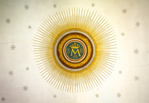 Monogram of the Blessed Virgin Mary, with crown, sun and stars on the background.
