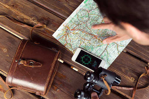 Hiker/Forester looking at his map while holding binoculars and using a compass application on his smartphone in Switzerland, Europe