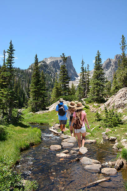 People with backpacks hiking on summer vacation in mountains. Father with his family enjoying time on a trip. Blue sky and high mountains in background. Rocky Mountain National Park, Colorado, USA.