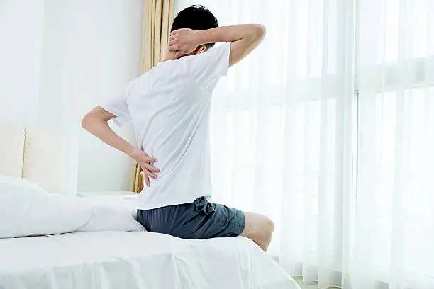 Young man sitting on the bed suffering from backpain.