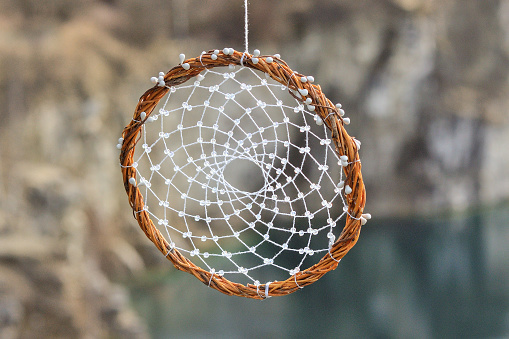 Handmade dream catcher on background of rocks and lake. Tribal elements, feathers