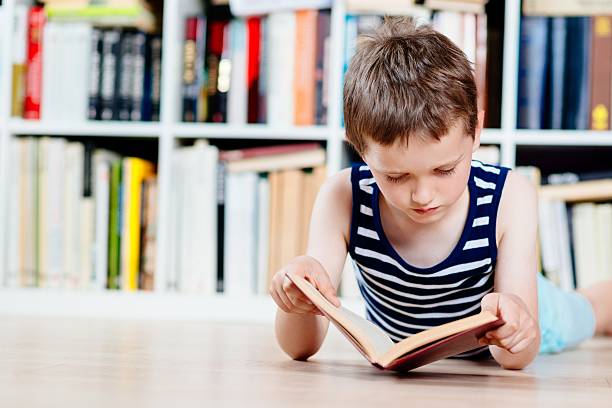 istock Seven years old boy reading a book in library. 610115488