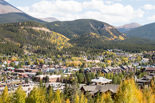 Looking down on the mountain town of Breckenridge, Colorado in the autumn.  There are many buildings in the small town surrounded by forest covered hills and mountains.