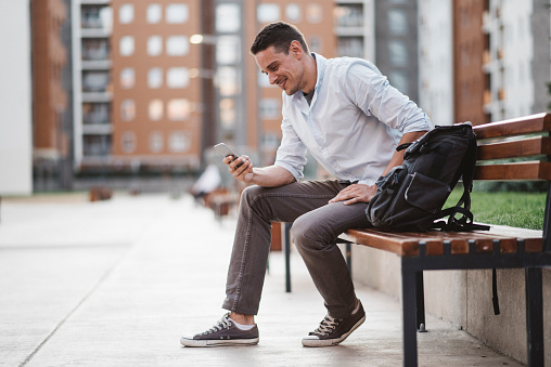 Smiling young man using smartphone on a park bench