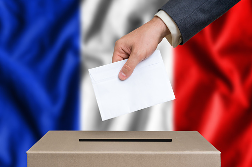 Election in France. The hand of man putting his vote in the ballot box. French flag on background.