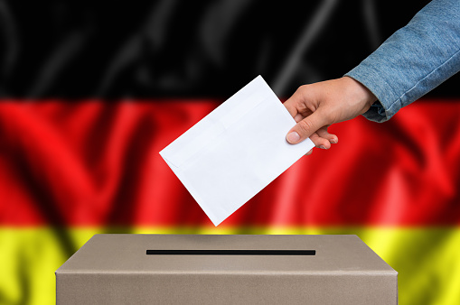 Election in Germany. The hand of woman putting her vote in the ballot box. German flag on background.