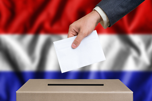 Election in Netherlands. The hand of man putting his vote in the ballot box. Dutch flag on background.