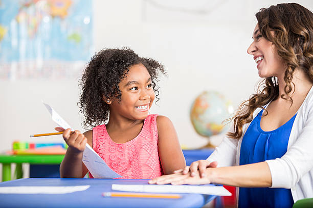 istock Smiling little girl working on homework with her cheerful teacher 610128730