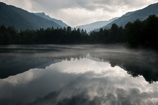mysterious lake in the mountains with reflected sky covered with mist