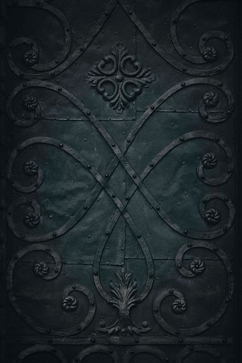 Dark, low key metal surface with decor from the exterior of an 18th century church door.
