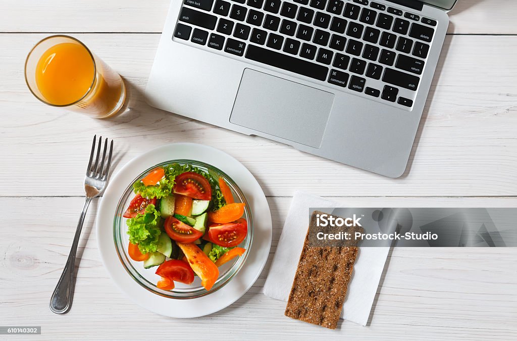 Healthy business lunch snack in office, vegetable salad top view Healthy business lunch in the office, top view of vegetable salad on white wooden desk near laptop computer keyboard. Salad bowl, juice, mobile phone and notepad with pen flat lay. Snack at break time Above Stock Photo