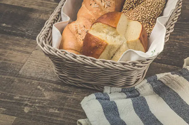 A professional DSLR photo of a grey rattan breadbasket with delicious crispy Austrian, German, Swiss buns. There are traditional buns inside the breadbasket like Salzstangerl, Kornspitz and a Laugenstangerl. Breadbasket is on a rustic old wooden table. Studio shot with professional equipment. Post processing with modern software.