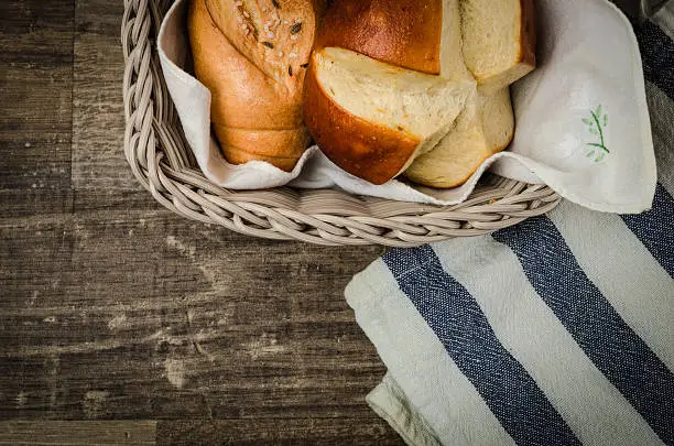 A professional DSLR photo of a grey rattan breadbasket with delicious crispy Austrian, German, Swiss buns. There are traditional buns inside the breadbasket like Salzstangerl, Kornspitz and a Laugenstangerl. Breadbasket is on a rustic old wooden table. Studio shot with professional equipment. Post processing with modern software.