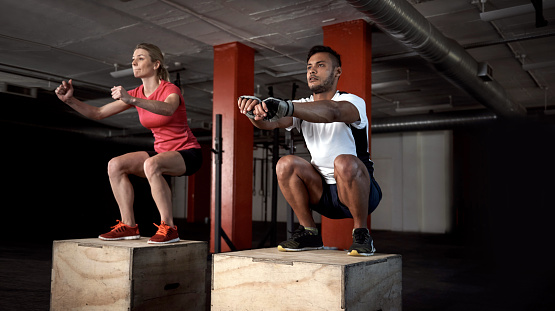 Shot of two people doing plyometric exercises on boxes