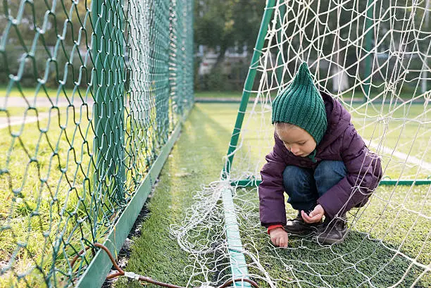 Little girl playing on a fooball pitch. She is sitting behind the goal.