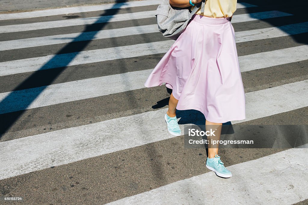 Girl in a pink skirt and sneakers crossing the road Girl in a pink skirt and sneakers crossing the road in the summer Skirt Stock Photo