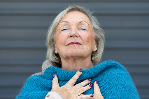 Attractive senior woman savoring the moment standing with her eyes closed and head tilted back with a serene expression as she clasps her chest with her hands