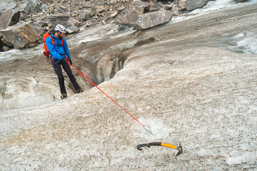Male guide in 20s anchors a metal ring into the ice and begins to rappel down an icy slope into a moulin crevsse during a trekking adventure on Lemon Glacier, Juneau Icefield, Juneau, Alaska, USA