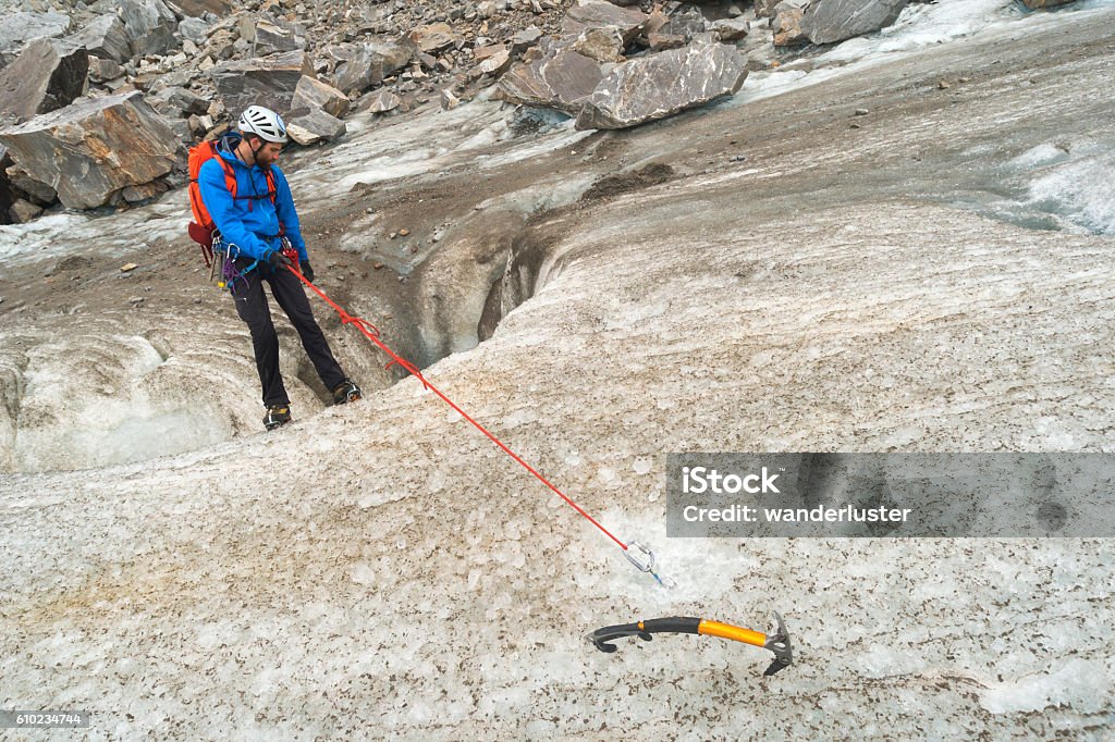 Man descends a moulin Male guide in 20s anchors a metal ring into the ice and begins to rappel down an icy slope into a moulin crevsse during a trekking adventure on Lemon Glacier, Juneau Icefield, Juneau, Alaska, USA Crevasse Stock Photo