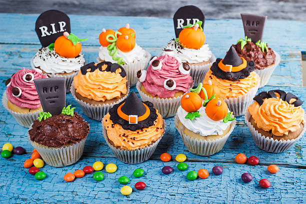 Halloween cupcakes with colored decorations Halloween cupcakes with decorations: Witches hat, eyes, tombstone and orange pumpkins made from confectionery mastic, wooden background halloween cupcake stock pictures, royalty-free photos & images