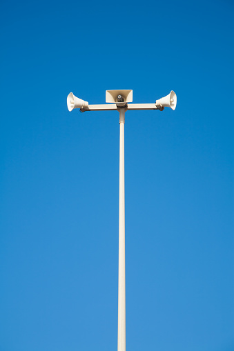white metal tall pole with three megaphones over blue sky outdoor