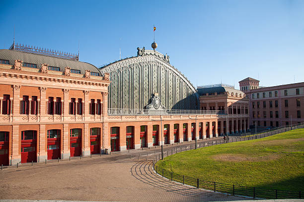landmark of facade building of Atocha public train station built in 1892 by Alberto de Palacio architect in Madrid city Spain Europe with spanish flag green grass field and blue clear sky
