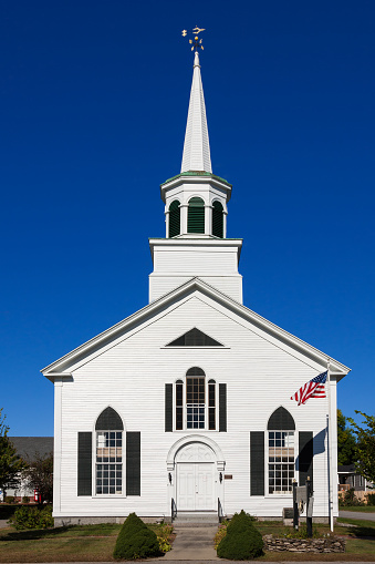 Wells, ME, USA - September 17, 2013: Congregational Church of Wells with White Clapboard Exterior, Wells, Maine, New England, USA. American flag, green bushes and vivid blue clear sky are in the image. Canon EF 24-105mm f/4 L IS lens. Polarizing filter