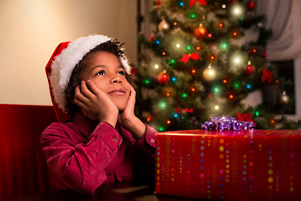 Afroamerican boy near Christmas present. Black kid beside Christmas present. Wait until it's time. Holiday for everyone.