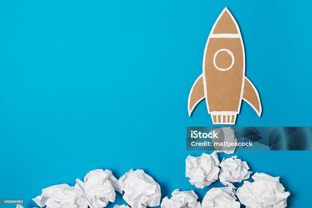 Creative boost A cardboard space rocket launching with crumped paper as clouds of smoke on a blue background. Growth Stock Photo