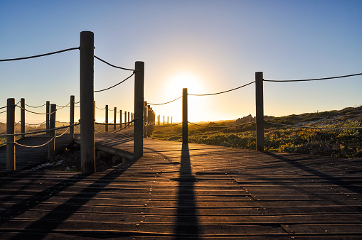 Sunset & walkway at Cape Agulhas (Cape of the Needles),South Africa,southernmost point of the African continent.It marks the division point between the Atlantic and Pacific Ocean.Lens flares from sun.