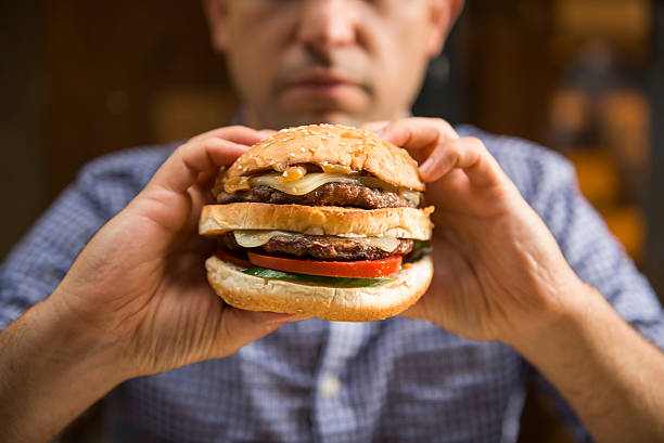 uomo in possesso di un grande hamburger - hamburger burger cheeseburger food foto e immagini stock