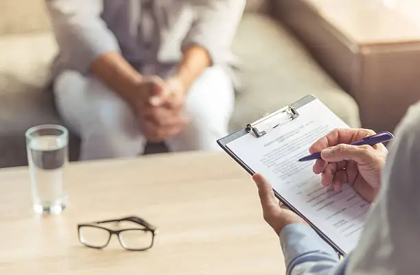 Cropped image of depressed man at the psychotherapist. Doctor is making notes while listening to his patient