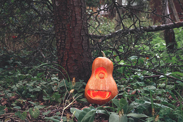 Halloween pumpkin minion in woods on grass near tree