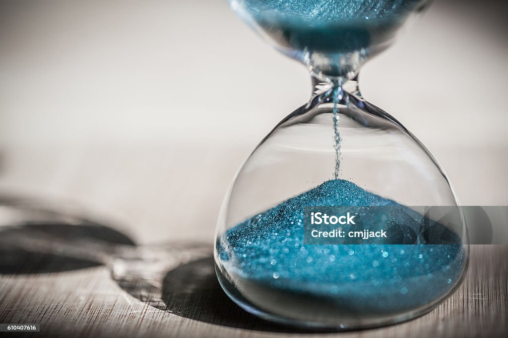 Sand running through the bulbs of an hourglass Sand running through the bulbs of an hourglass measuring the passing time in a countdown to a deadline, on a bright wooden background with copy space. Hourglass Stock Photo