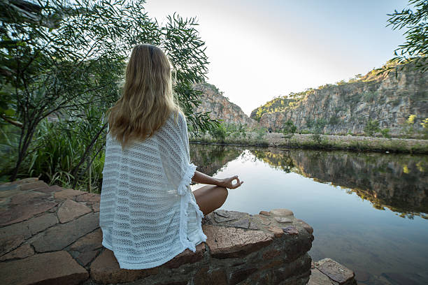 young woman by the lake exercises yoga in lotus position - zen like nature breathing exercise sitting imagens e fotografias de stock