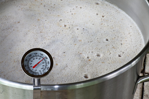 A dial thermometer measures the temperature of a mash used to make beer.