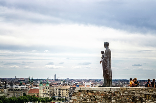 Budapest, Hungary - July 15, 2016: Statue overlooking the City of Budapest. Tourists are pictured on the parapet alongside