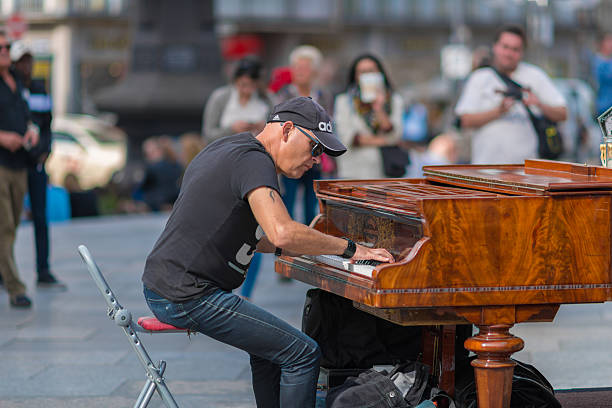 Hamburg, Germany - March 17. 2018: A young man is playing a transportable piano in the shopping arcade in Hamburg city. street musicians playing for money or entertainment. in the background are walking passers-by, as well as various shops such as o2. The picture was cross developed.