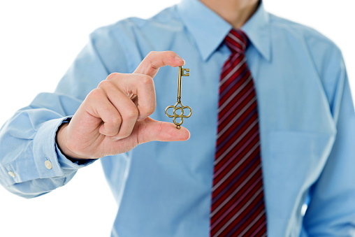 Closeup of businessman handing key against white background.