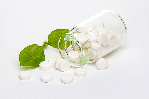 White pills in clear glass container with green leaf stock photo