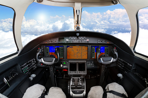 Corporate Jet Cockpit view above clouds with blue sky, sun and no pilots