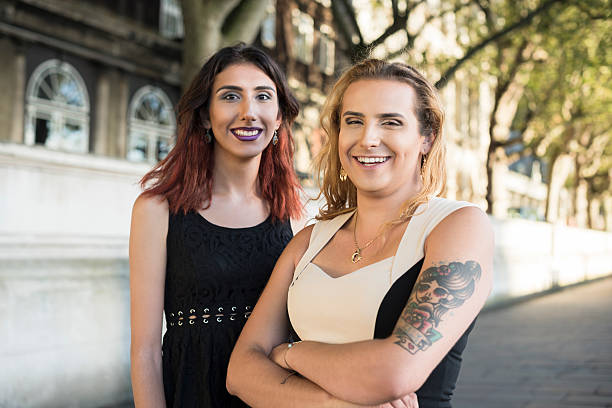 Portrait of two transgender female friends smiling Transgender female with arms folded and tattoo with  friend, standing outdoors, smiling transgender person photos stock pictures, royalty-free photos & images
