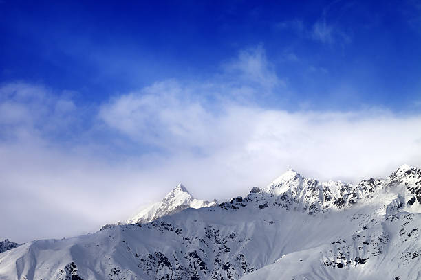 istock Snow sunlight mountain peak in fog and blue sky 610449244