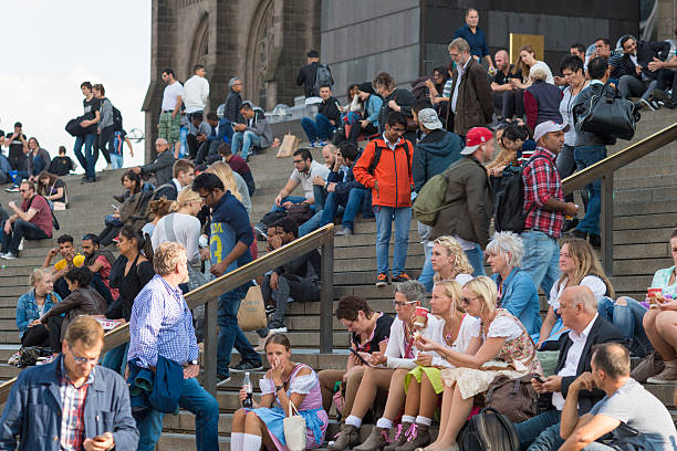 Cologne, Germany - September 23, 2016: The Cologne Cathedral is a meeting point for a lot of people in summer. They sitting on the steps to the Cathedral, talking together, looking at smartphones or waiting for the train in the Central Station Koln nearby. 
