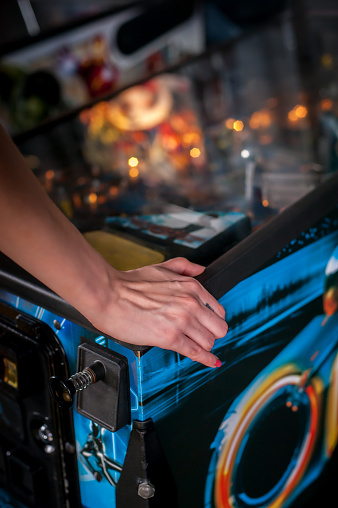 Hand of female pressing button and playing pinball machine