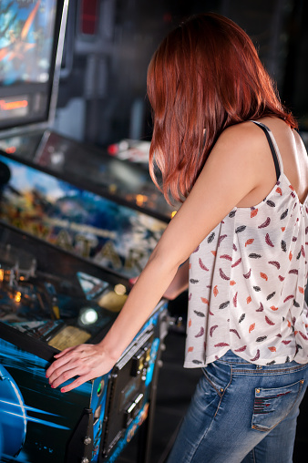 Young woman playing on the pinball machine in game room
