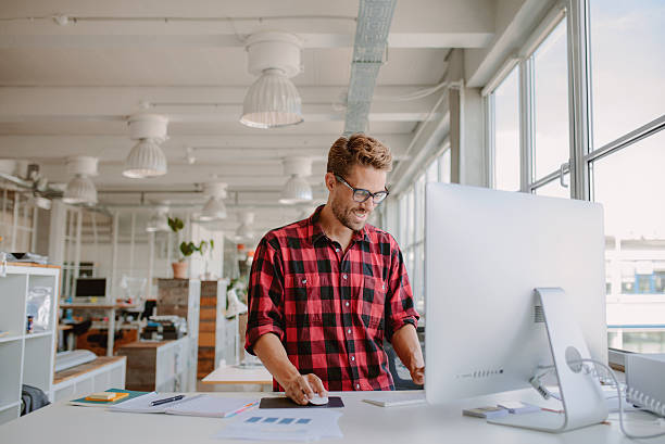 Young man working in modern workplace Shot of happy young man working on desktop computer in modern workplace. Young entrepreneur working at start up. graphic designer stock pictures, royalty-free photos & images